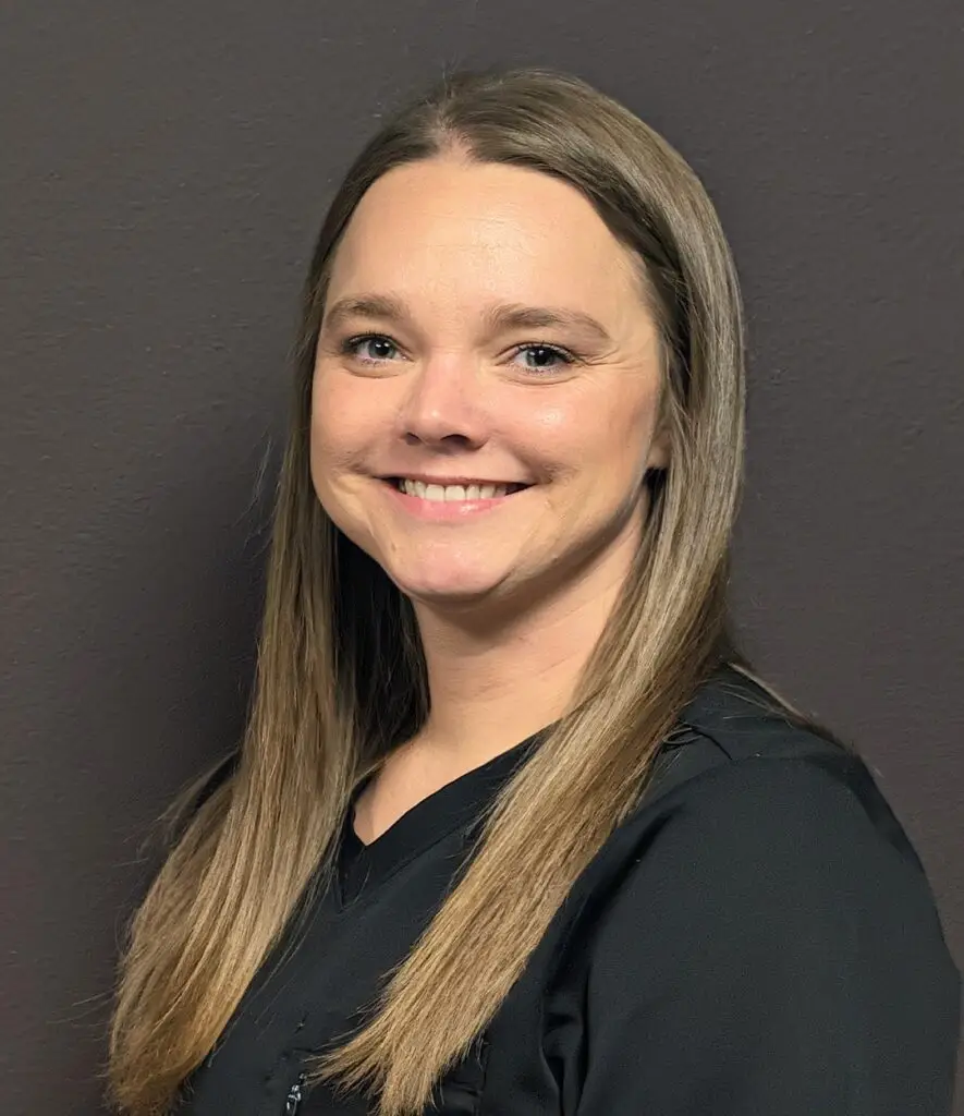 Headshot of a Female nurse with long blonde hair in a black scrub top smiling