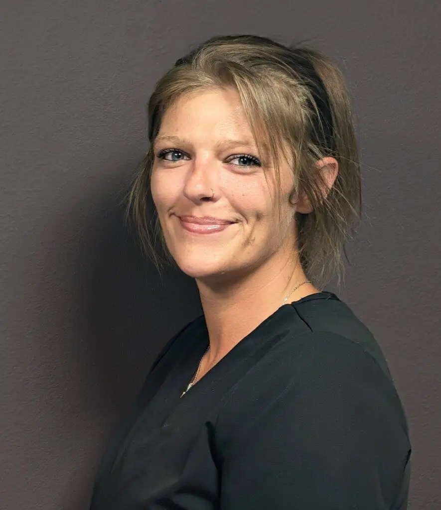 Headshot of a Female nurse with long auburn hair in a black scrub top